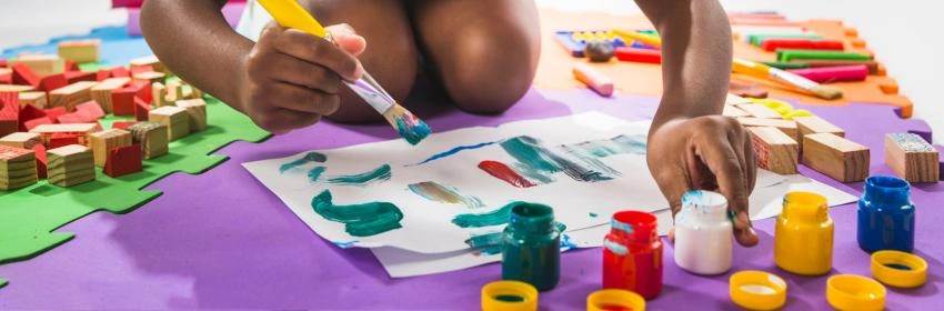 criança-brincando-no-chão-com-várias-tintas-e-pincéis-coloridos